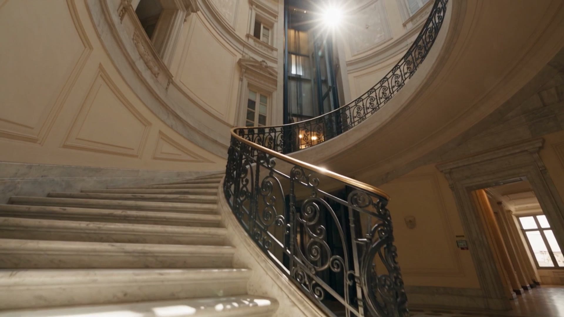 La scala elicoidale di un palazzo storico con l'ascensore di vetro al centro