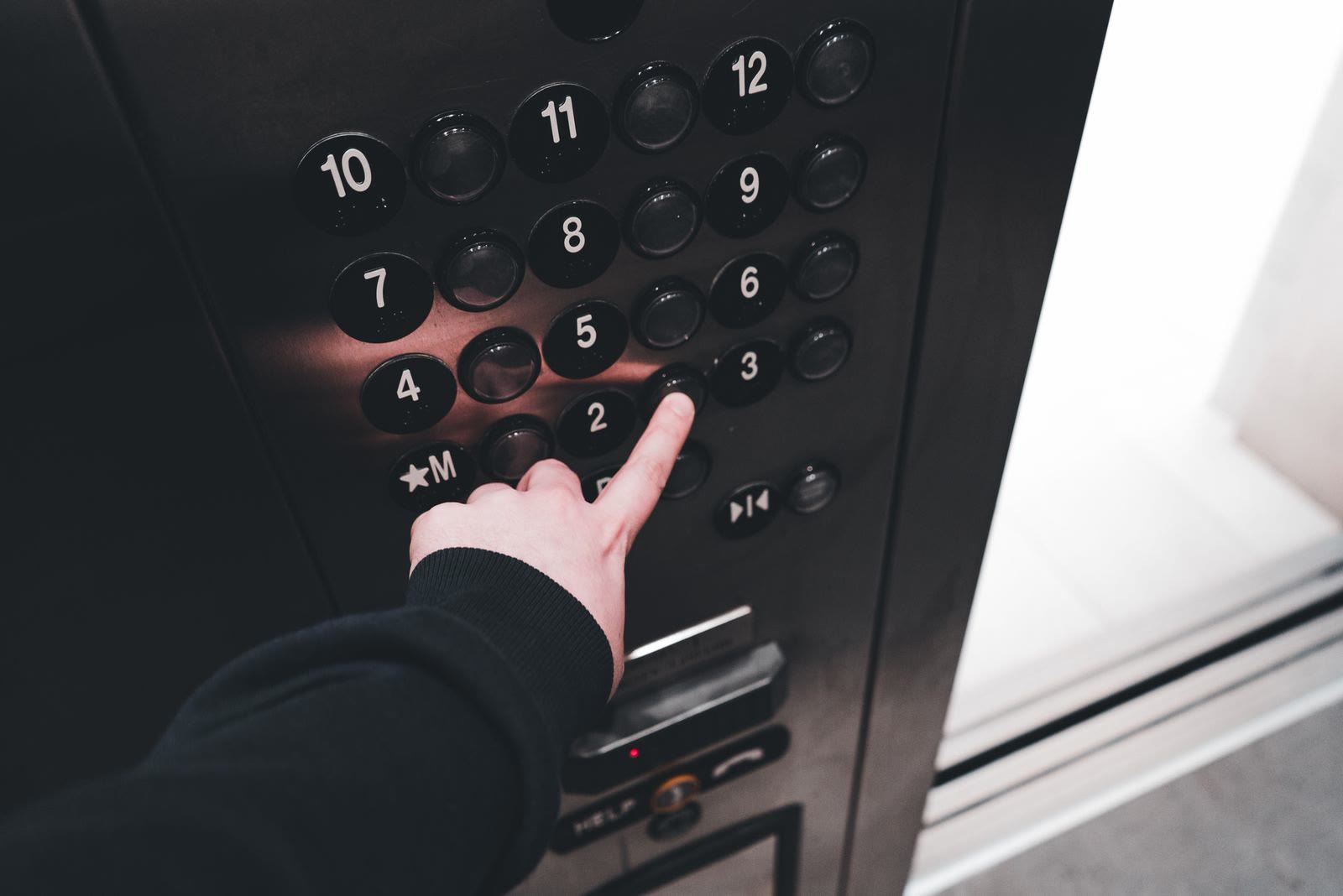 Una mano preme il pulsante di una pulsantiera di cabina