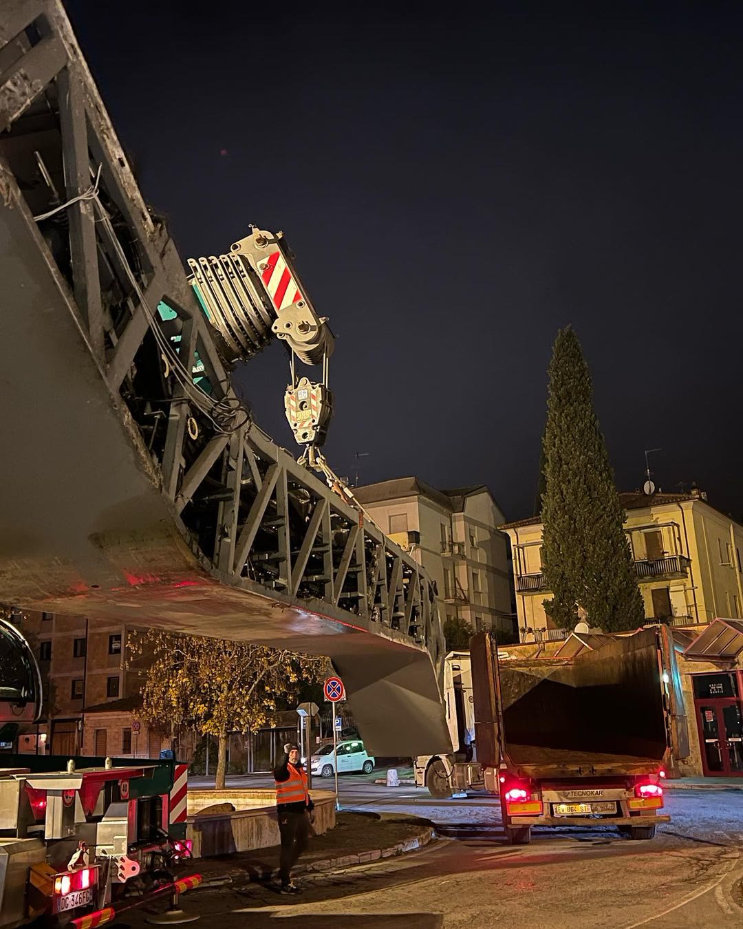 L'autogru che solleva il traliccio di una scala mobile in una piazza di notte